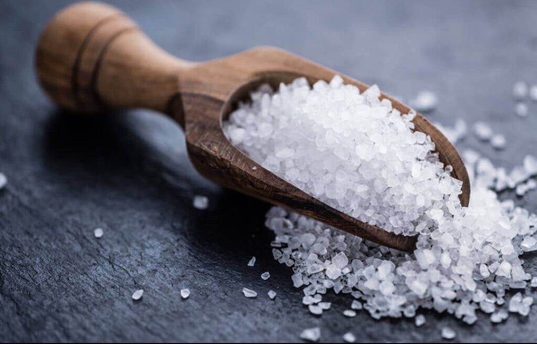 Salz in einem kleinen Holzdosierer auf einer schwarzen Holzplatte. 